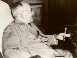 Getúlio Vargas sentado, de terno, tendo à mão um charuto.