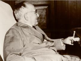 Getúlio Vargas sentado, de terno, tendo à mão um charuto.